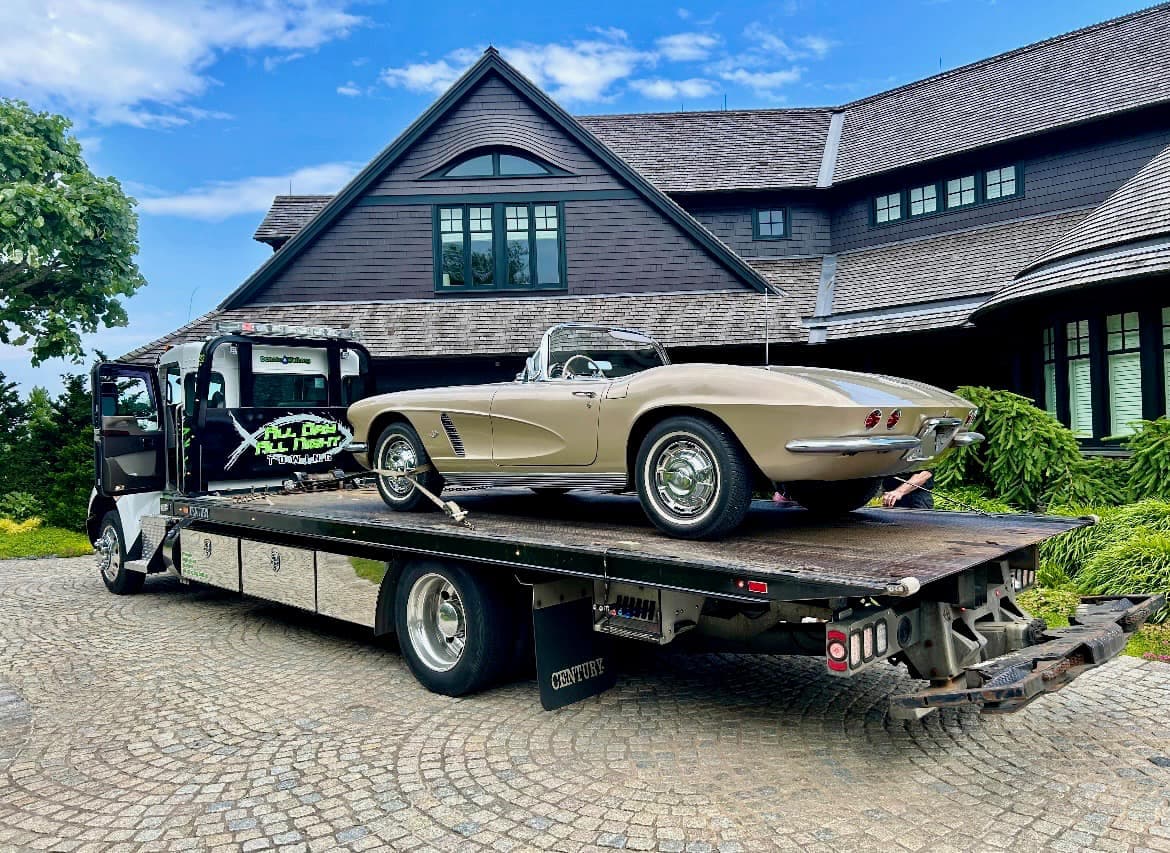 White-cab flatbed tow truck carrying a classic Corvette convertible