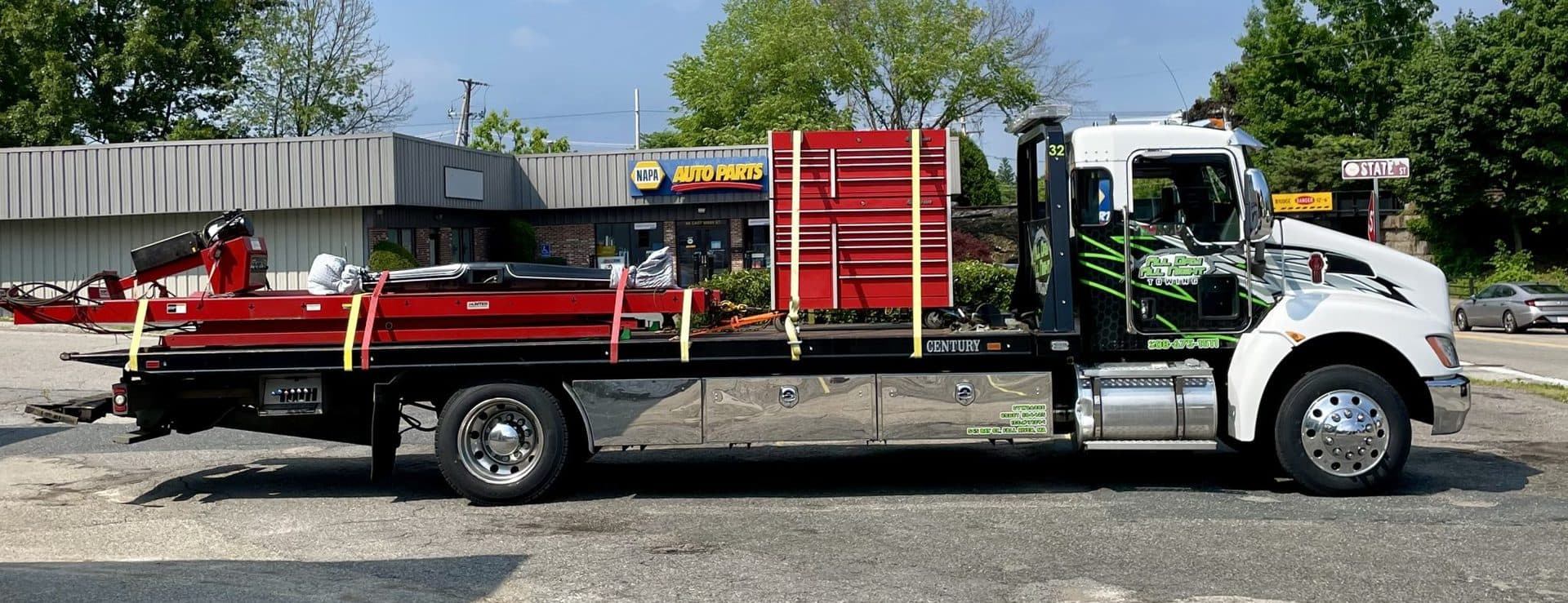 Flatbed tow truck in side profile, loaded with shop equipment