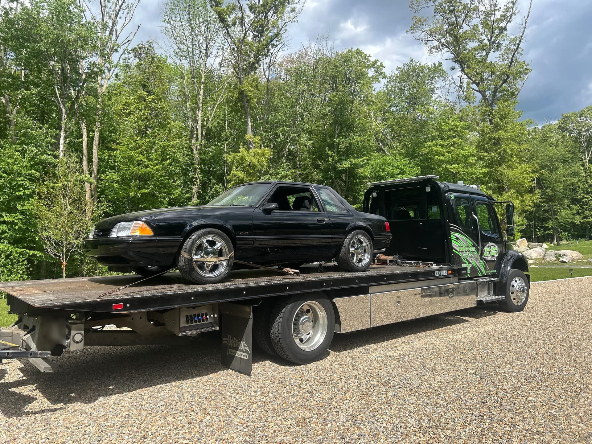Black-cab flatbed tow truck carrying a classic Mustang